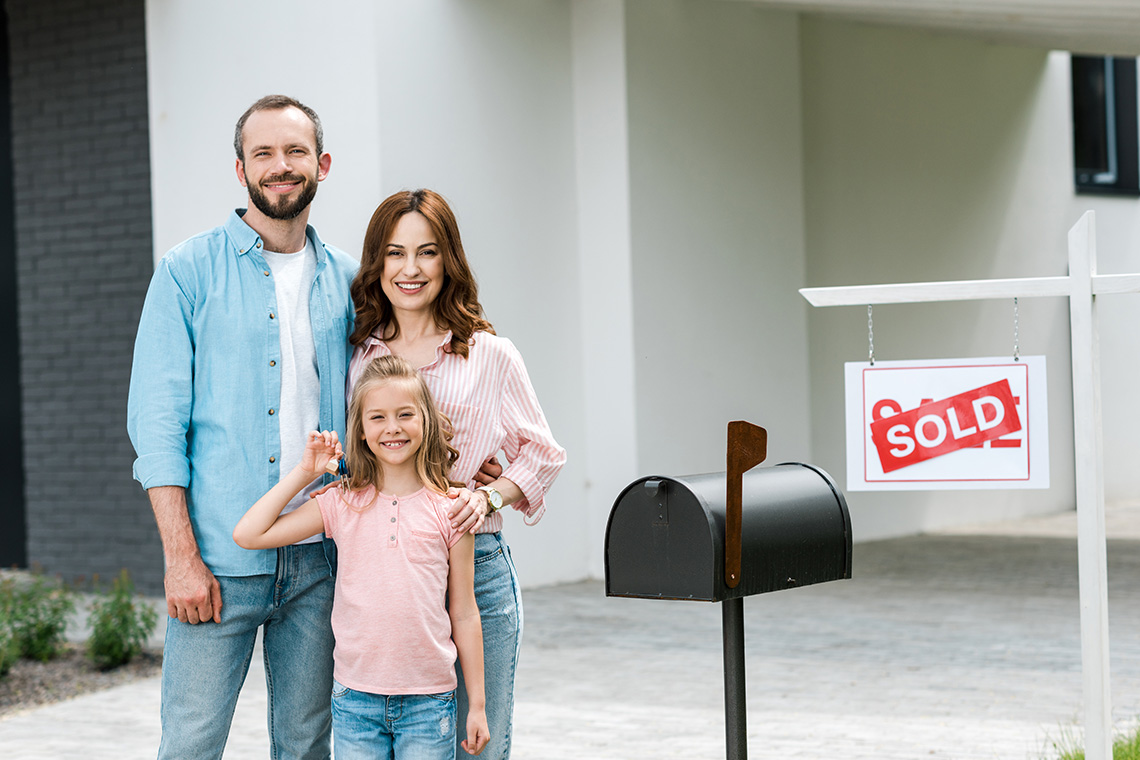 family by mailbox in front of house with sold sign